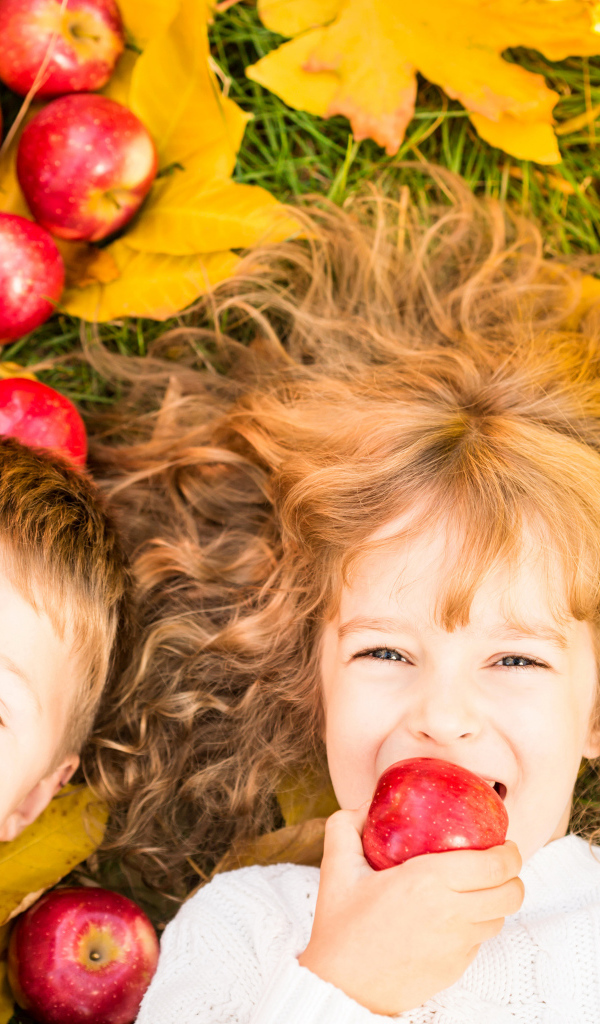 Маленькие мальчик и девочка лежат на желтой листве с красными яблоками