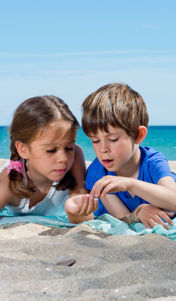 Маленькие мальчик и девочка играют на песке у моря