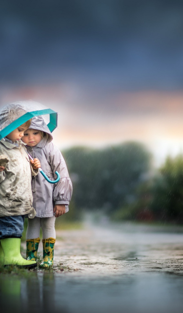 Маленькие мальчик и девочка под зонтом на дороге 