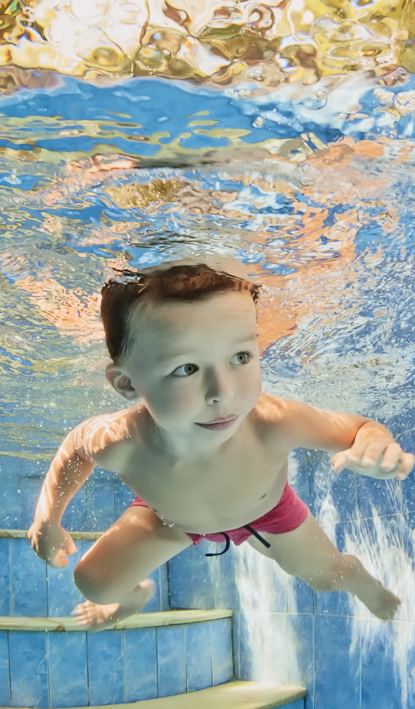 Маленький мальчик плавает под водой в бассейне