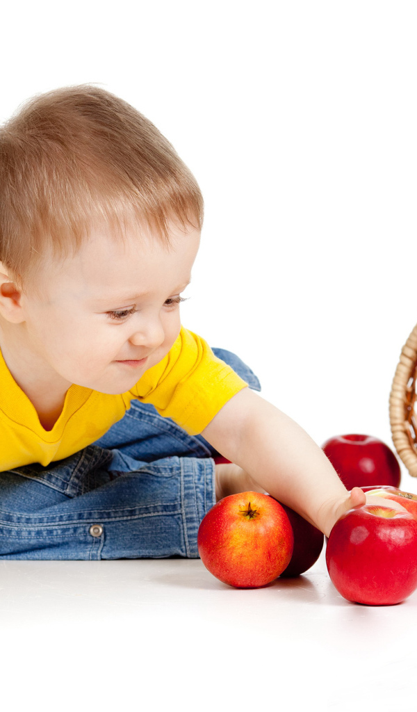 Маленький мальчик с корзиной спелых яблок на белом фоне