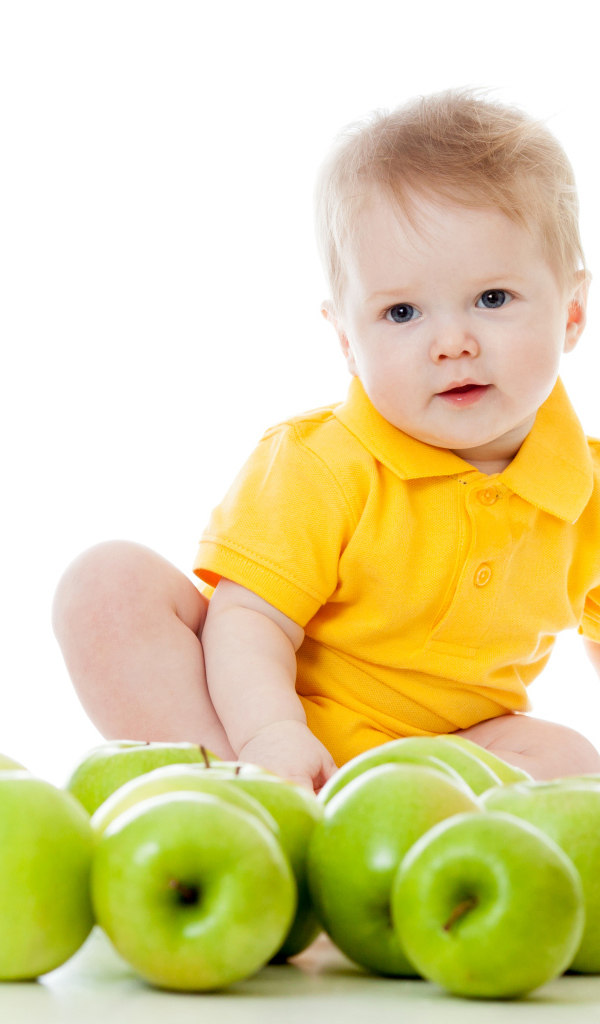 Маленький мальчик с зелеными яблоками на белом фоне