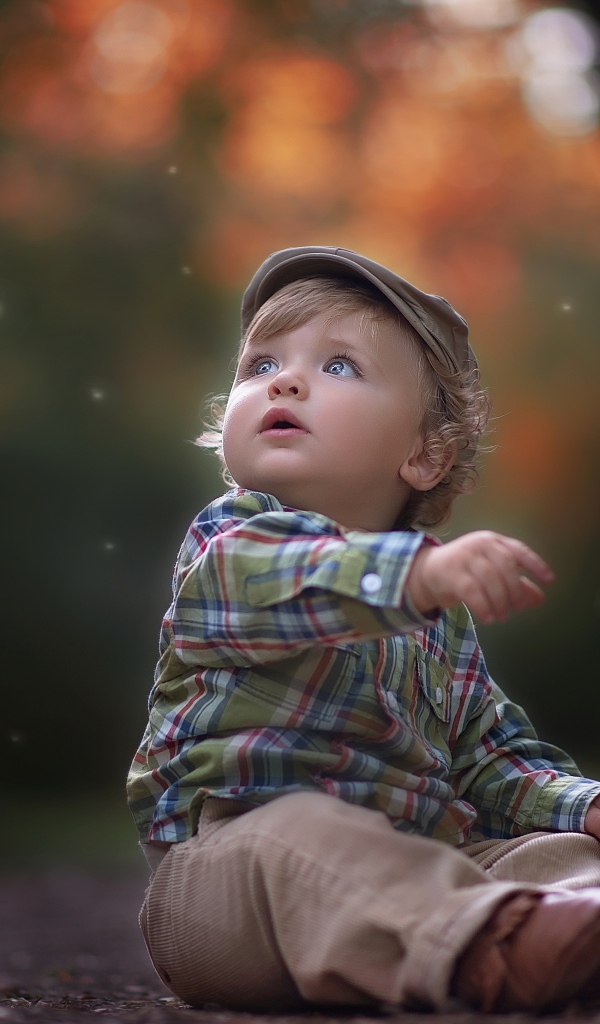 Маленький милый мальчик сидит в кепке на дороге