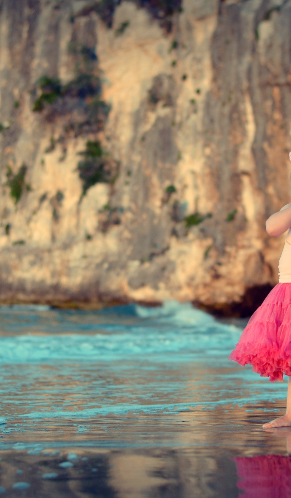 Маленькая девочка в красивой розовой юбке на пляже