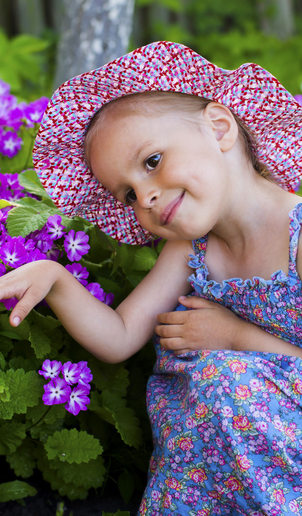 Маленькая девочка в шляпе рядом с фиолетовыми цветами