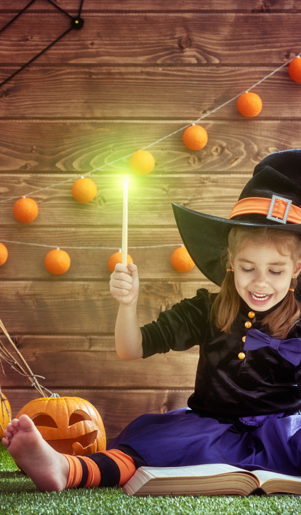 Маленькая девочка в костюме ведьмы с волшебной книгой на Хэллоуин