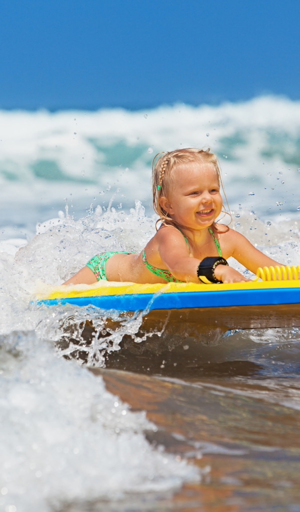 Маленькая девочка в море на доске для серфинга