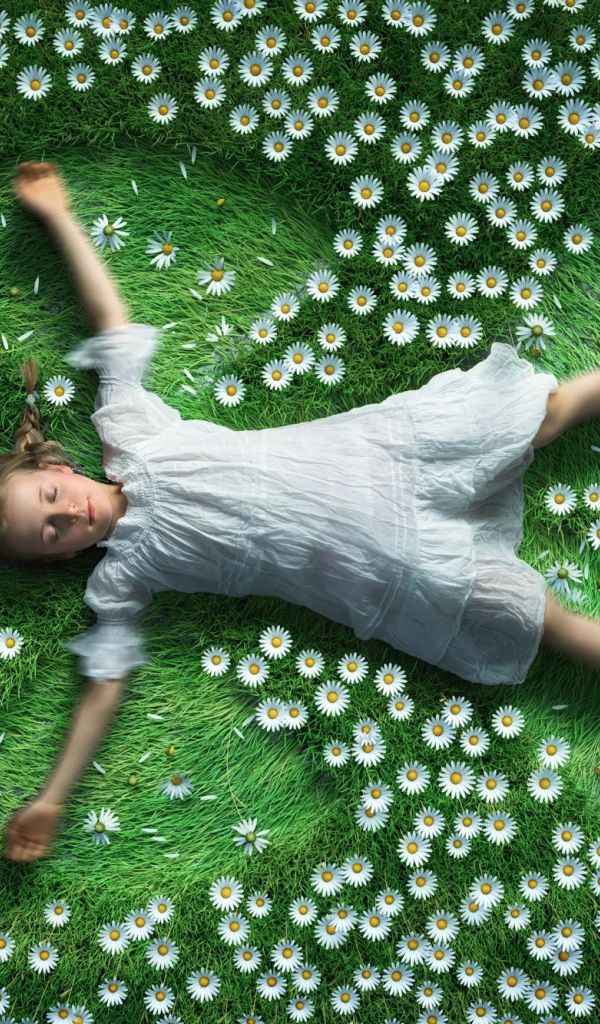 Маленькая девочка в белом платье лежит на зеленой траве с ромашками