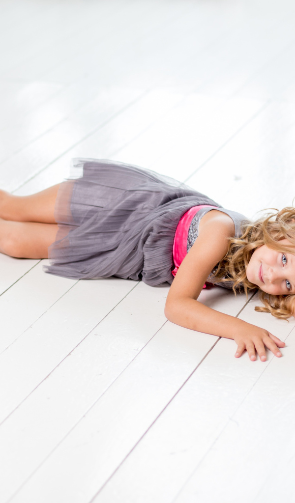 Маленькая девочка модель в сером платье лежит на деревянном полу