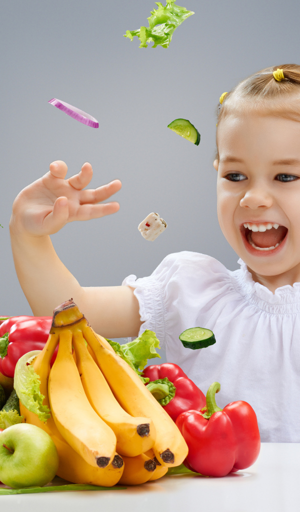 Маленькая девочка играет с овощами и фруктами на кухне