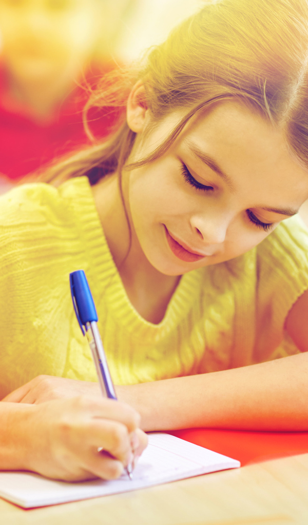 Маленькая девочка школьница пишет ручкой в тетради