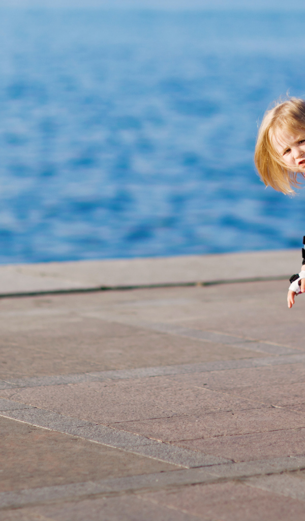 Маленькая девочка катается на роликах на побережье