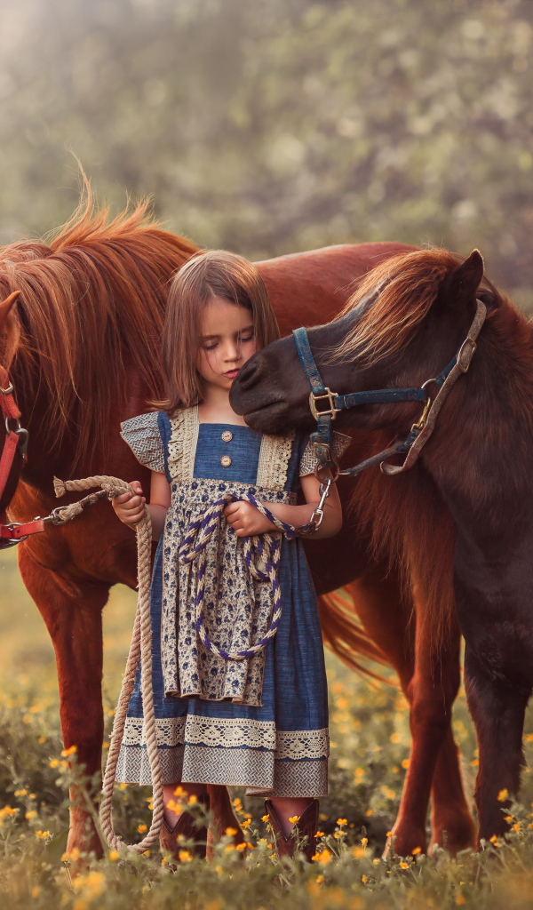 Маленькая девочка гуляет по полю с маленькими пони