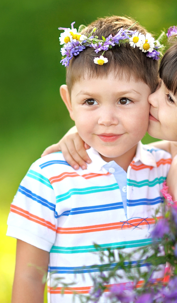 Маленькая девочка с букетом полевых цветов целует мальчика