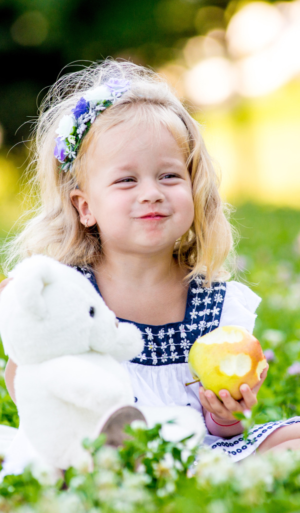 Маленькая девочка с белым медвежонком в руках и большим яблоком
