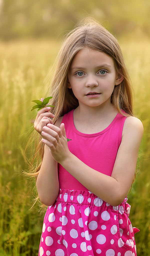 Маленькая длинноволосая девочка в розовом сарафане на поле