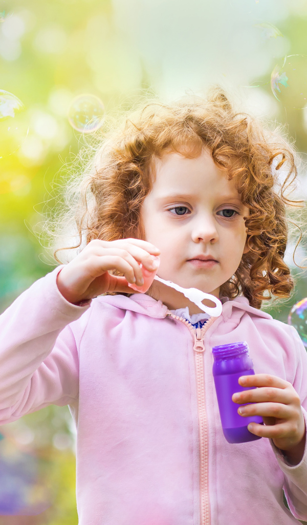 Маленькая рыжеволосая кудрявая девочка с мыльными пузырями