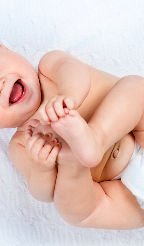 Маленький улыбающийся грудной ребенок держит руками ноги