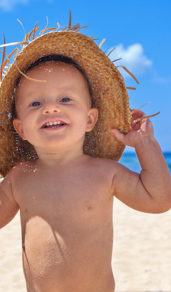 Маленький улыбающийся мальчик в соломенной шляпе на пляже