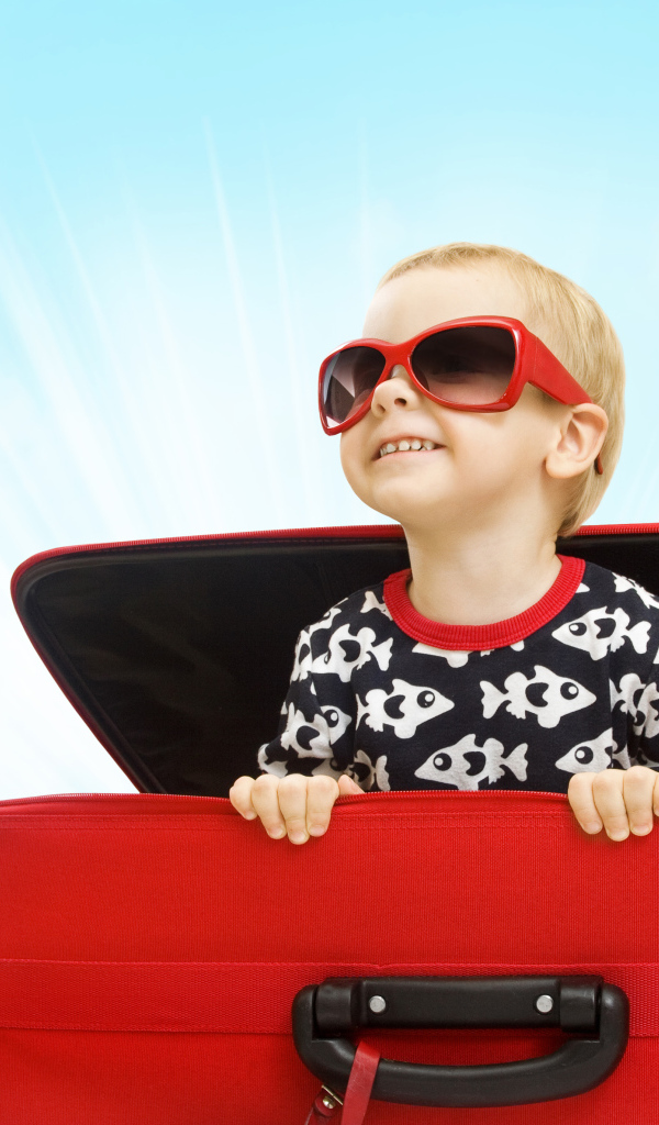 Маленький улыбающийся мальчик в очках сидит в красном чемодане