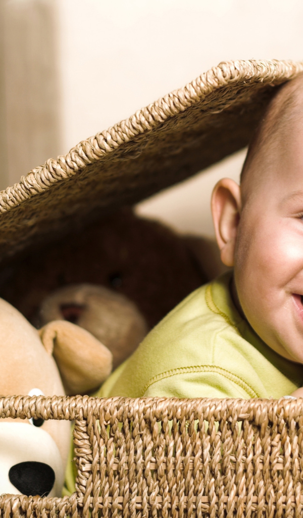 Маленький улыбающийся ребенок сидит в корзине с игрушками