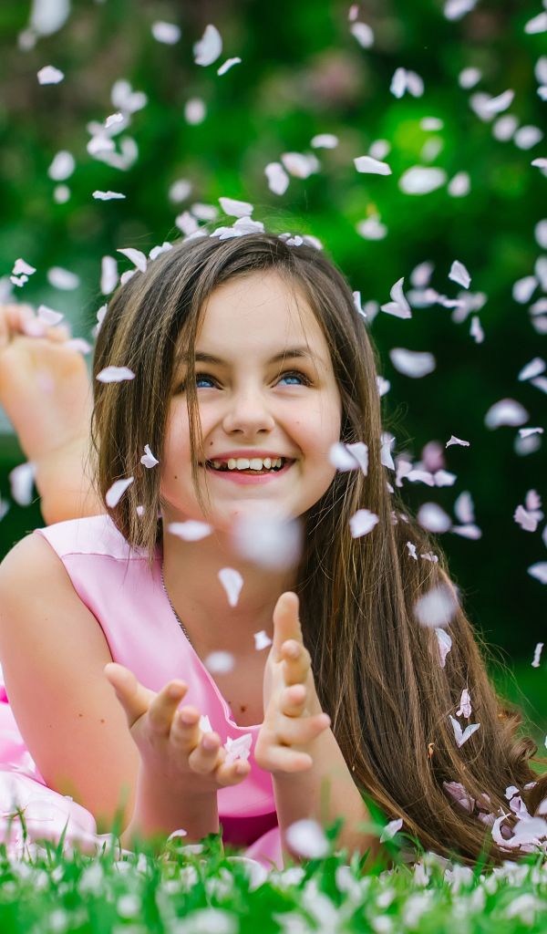 Маленькая улыбающаяся девочка шатенка ловит лепестки