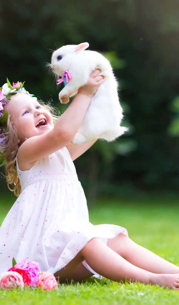 Маленькая улыбающаяся девочка держит в руках белого кролика