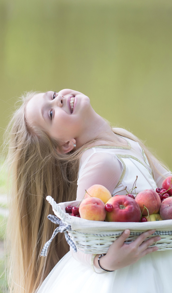 Маленькая улыбающаяся девочка в белом платье с корзиной фруктов