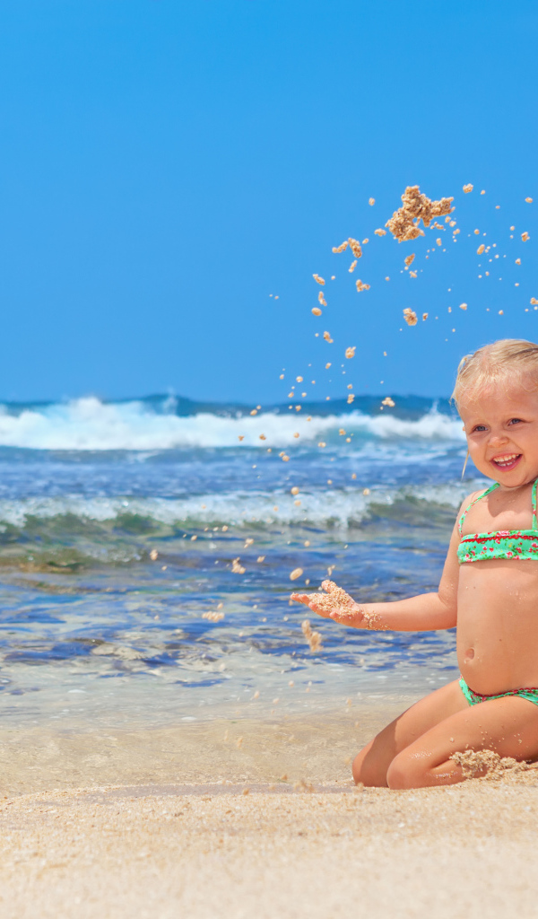 Маленькая улыбающаяся девочка играет на пляже с песком