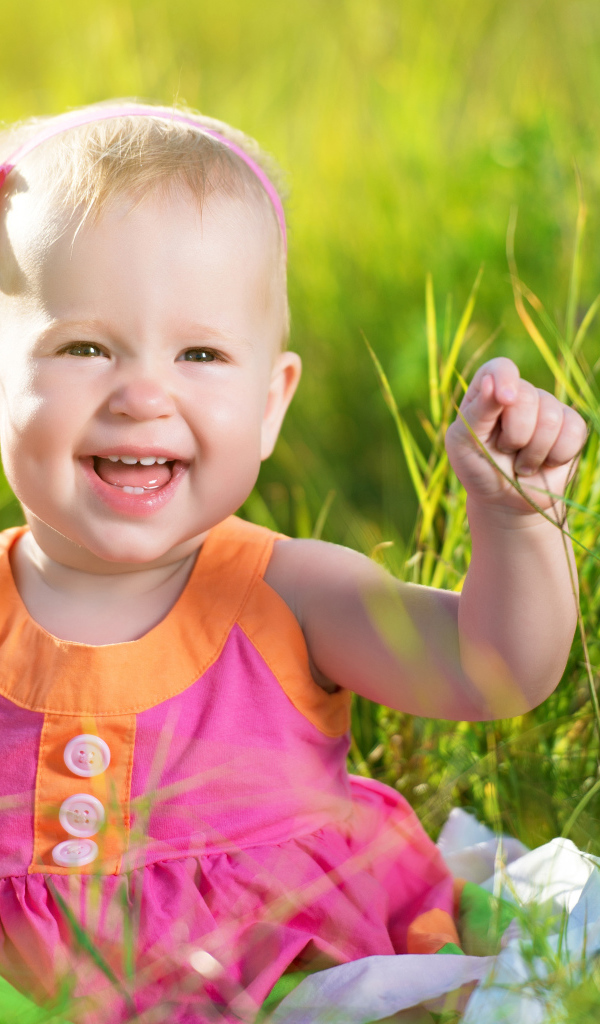 Маленькая улыбающаяся девочка сидит в зеленой траве