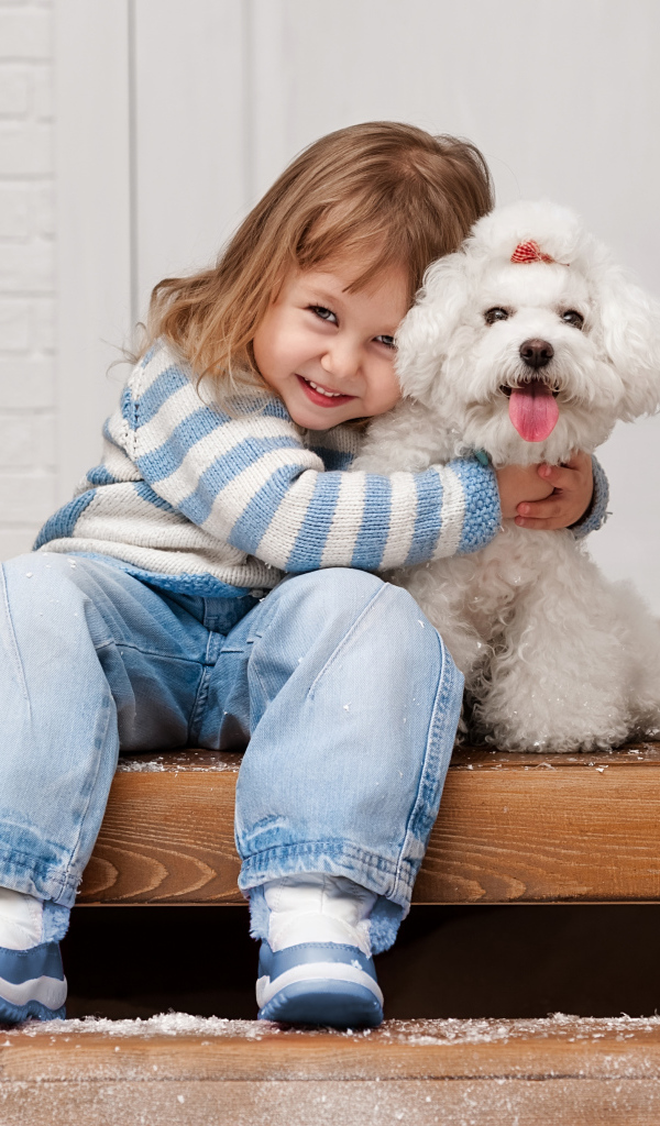 Маленькая улыбающаяся девочка сидит с белым пуделем на ступеньках