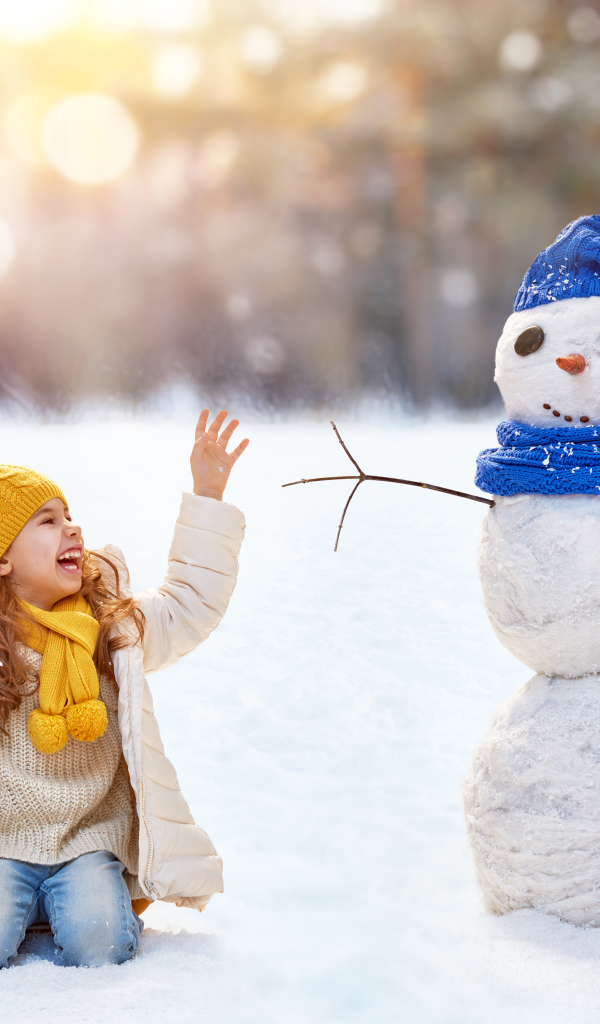 Маленькая улыбающаяся девочка со снеговиком зимой