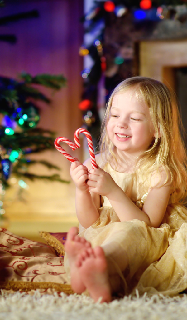 Длинноволосая девочка блондинка с леденцами у новогодней елки