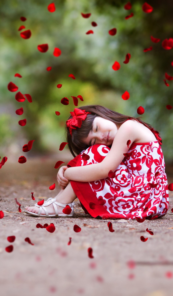 Лепестки красной розы падают на маленькую девочку