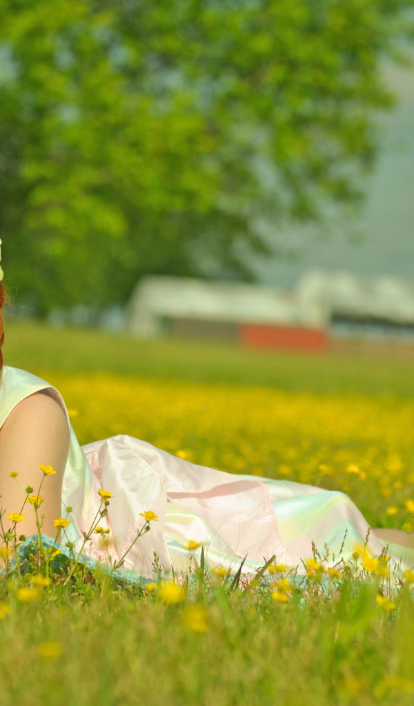 Рыжеволосая девочка с косичками лежит на зеленой траве