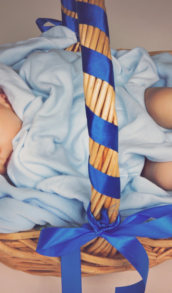 Спящий грудной ребенок в корзине с синими лентами