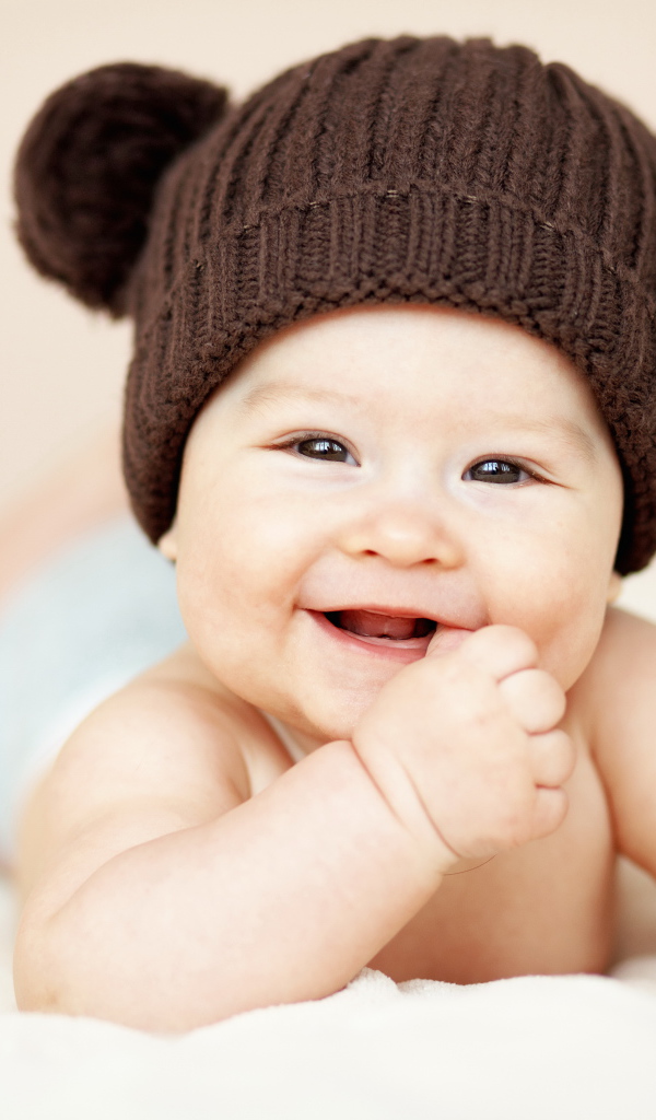 Улыбающийся грудной ребенок в коричневой вязаной шапке