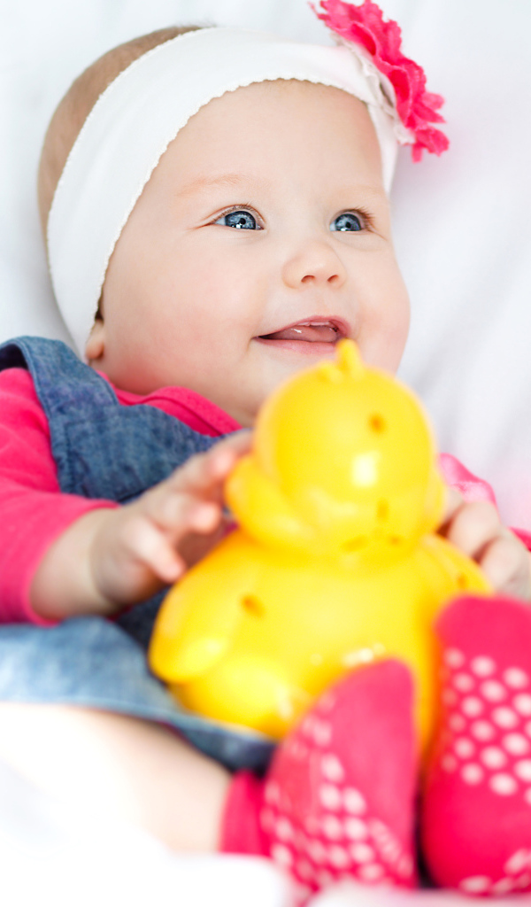Улыбающаяся голубоглазая девочка младенец с игрушкой в руках
