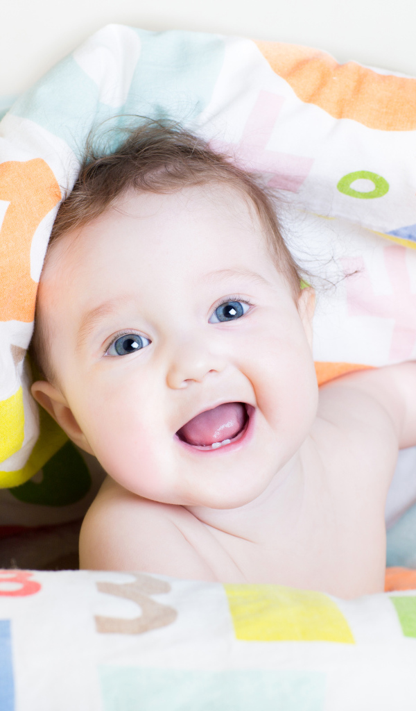 Улыбающийся голубоглазый ребенок под разноцветным покрывалом