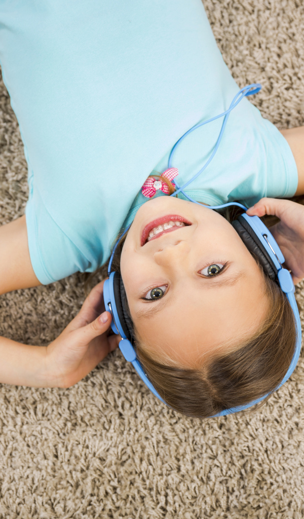 Улыбающаяся девочка в больших голубых наушниках