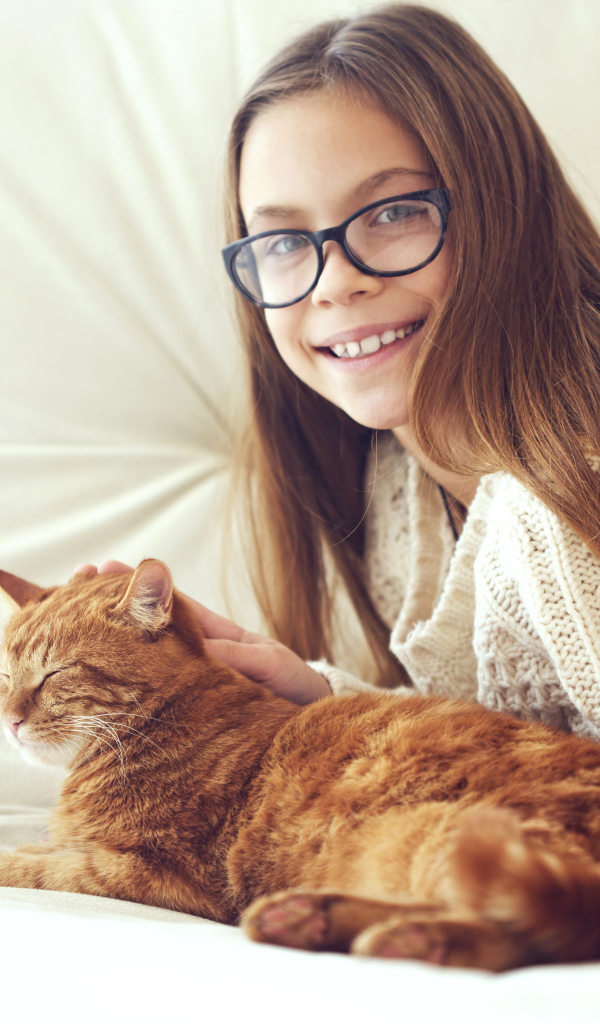 Улыбающаяся девочка шатенка в очках гладит рыжего кота