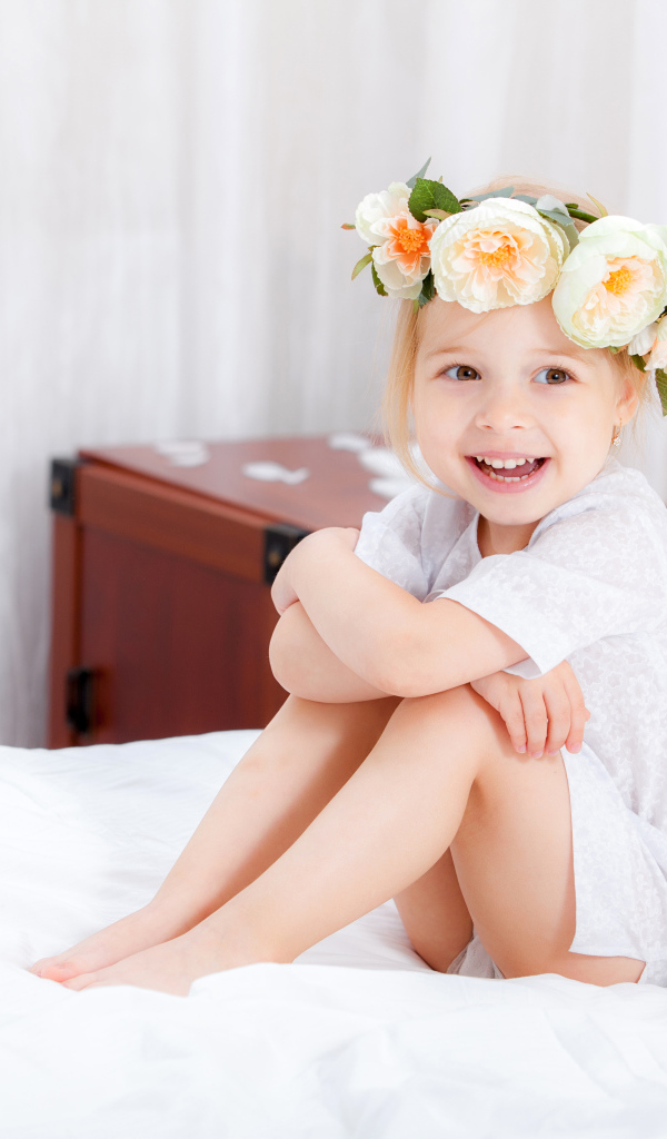 Улыбающаяся девочка с венком на голове сидит на кровати