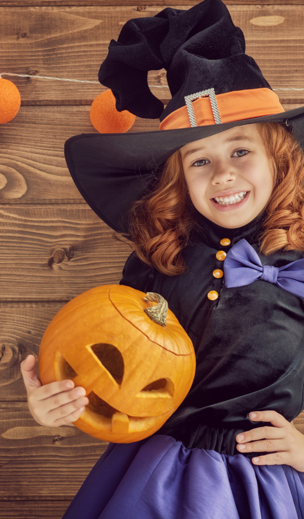 Улыбающаяся маленькая девочка в костюме ведьмы с тыквой на Хэллоуин