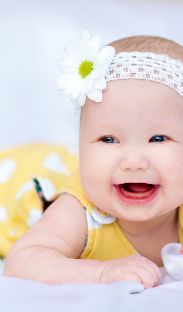 Улыбающаяся маленькая девочка в повязке с белым цветком на голове