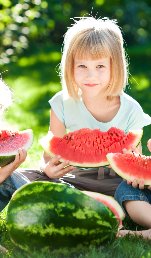 Три маленькие девочки едят арбуз на зеленой траве летом
