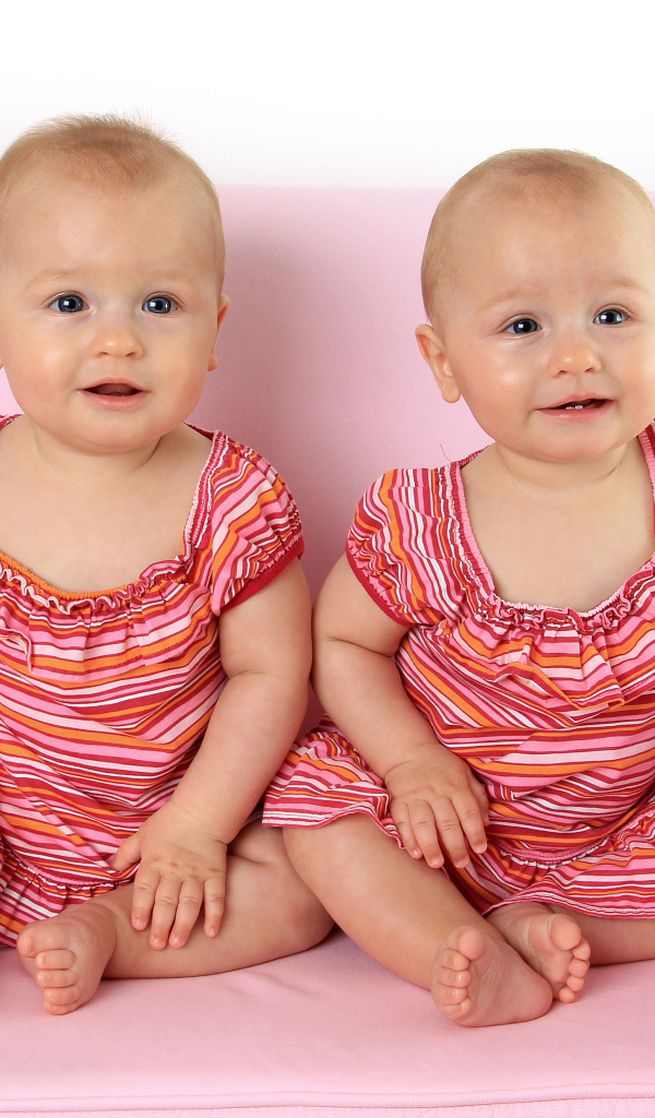 Две милые маленькие девочки сидят на розовом диване