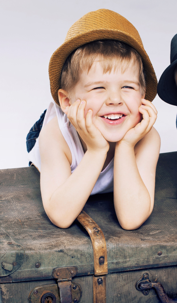 Два маленьких улыбающихся мальчика лежат на старом чемодане