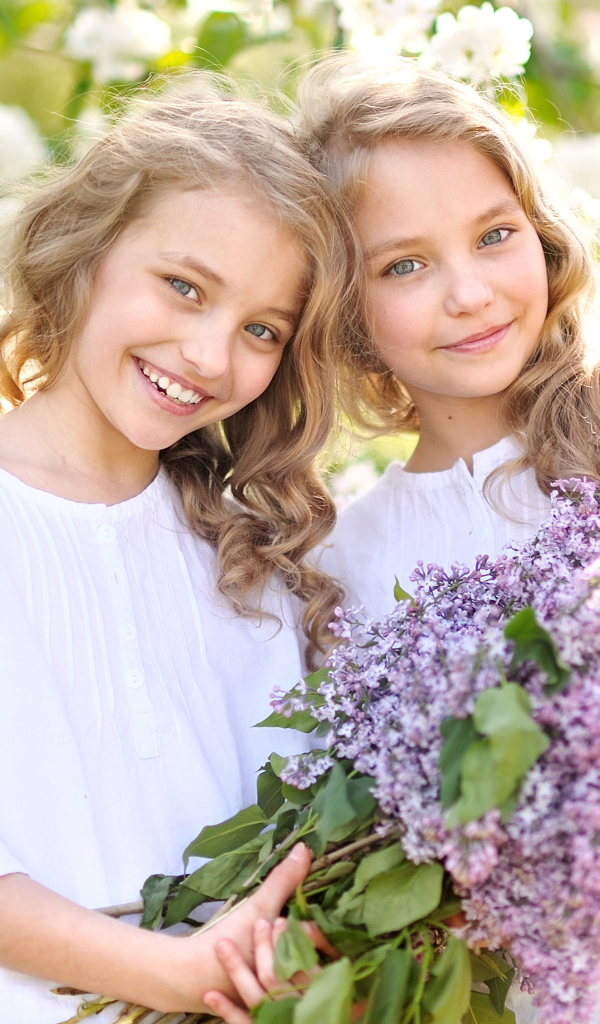 Две улыбающиеся девочки близняшки с букетом сирени