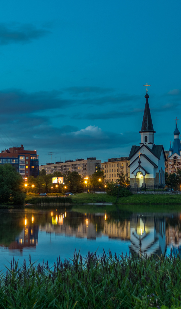 Вечерние огни маленькой церкви и домов отражаются в воде городского пруда, Санкт-Петербург. Россия