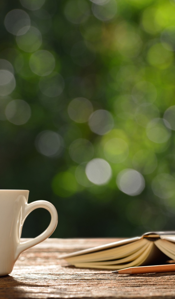 Белая чашка на столе с открытой книгой